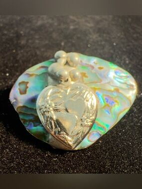 Artisan heart-shaped silver-tone brooch set against a piece of abalone shell.